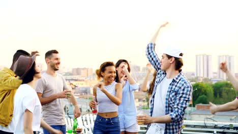la juventud moderna está bailando en la azotea disfrutando de la música mientras su amigo dj está mezclando trabajando con equipos con auriculares. fiesta, celebración y concepto divertido.