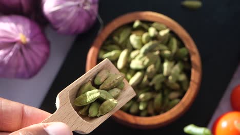 green cardamom pods in a wooden bowl with a wooden spoon