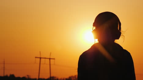 Silueta-De-Un-Adolescente-En-Los-Auriculares-Contra-El-Fondo-De-La-Ciudad-Y-El-Atardecer