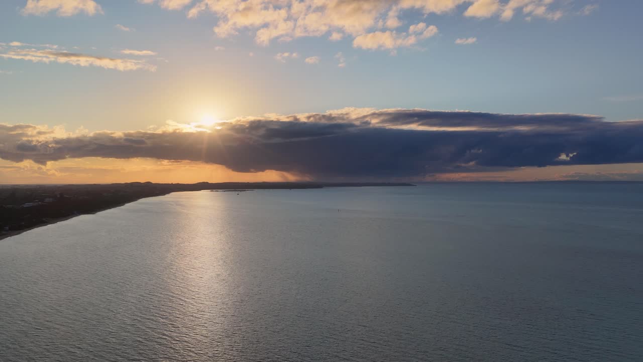 Drone captures tranquil sunset over ocean with dramatic clouds, soft golden light, and gentle movement