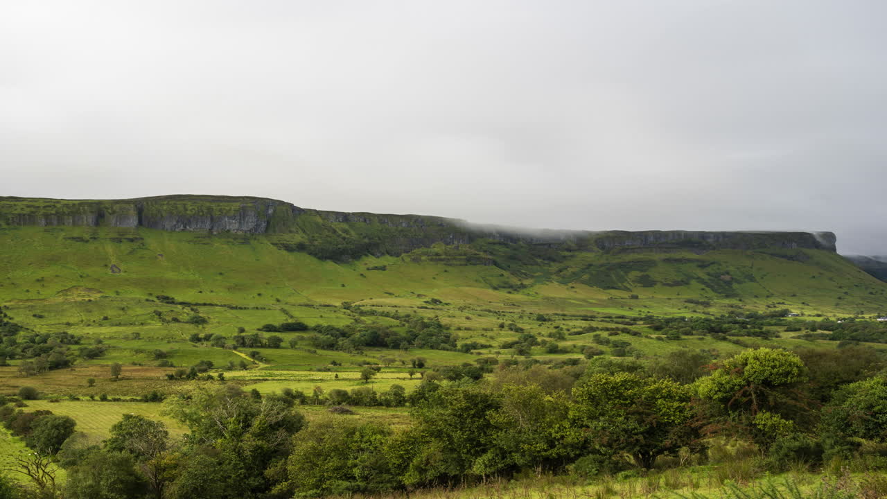 lapso de tiempo de la niebla de la mañana rodando sobre las verdes colinas y el paisaje de árboles en primer plano en el campo rural de irlanda