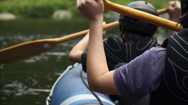 Two white kids paddle canoe with helmets and pfd on Pelorus river, New Zealand with beautiful nature in background - behind shot