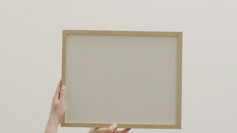 manos de una mujer caucásica sosteniendo un marco con espacio de copia en fondo blanco contra una pared blanca