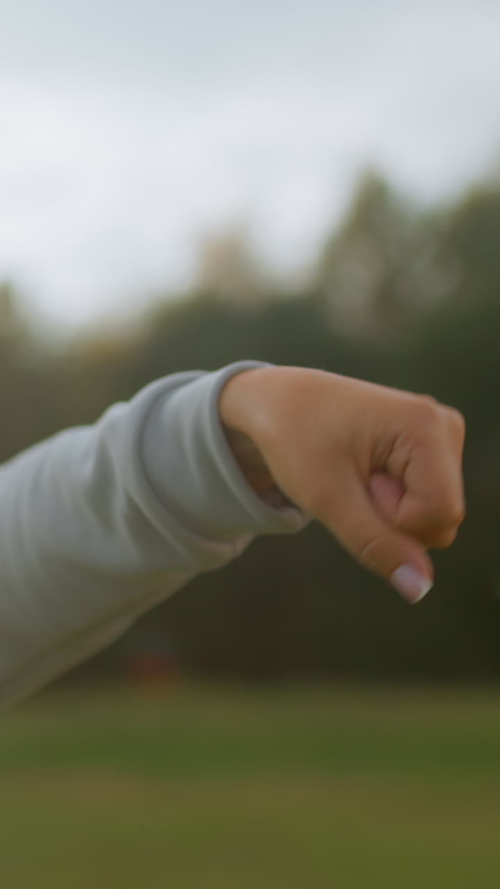 주먹을 꽉 쥐고 팔뚝을 회전하는 동작을 보여주는 팔의 클로즈업, 따뜻한 역광, 스웨트셔츠 소매, 풀이 무성한 들판 배경, 피트니스를 위한 신중한 훈련 리듬 및 기술에 집중하는 모습이 담긴 야외 장면