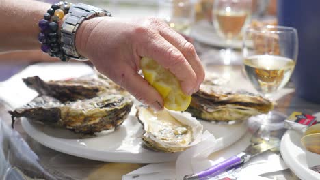 close-up of a tray of fresh oysters, with the left hand picking up the lemon in the middle and squeezing it onto an open oyster before tasting it