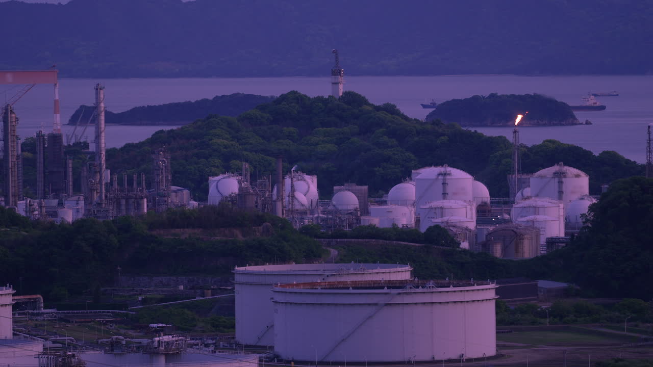 Industrial plant with smoking chimneys and burning flare stacks at dusk.