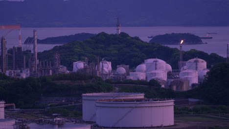 industrial plant with smoking chimneys and burning flare stacks at dusk.