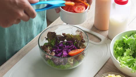 vista superior de un hombre haciendo ensalada poniendo tomate cortado en un tazón de ensalada