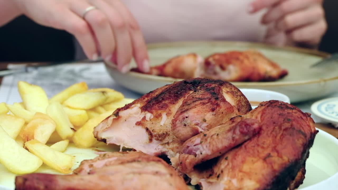 Woman cutting up a piece of grilled chicken with potatoes at a restaurant