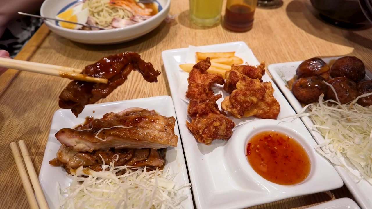 Jepretan close-up sumpit mengangkat ayam teriyaki dari piring saji di atas meja kayu.