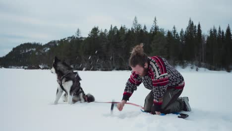 man breaking frozen lake using a hatchet axe to make a hole for ice fishing