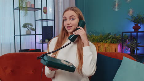 Girl-making-retro-telephone-from-90s-conversation-with-friends-sitting-call-on-couch-at-home-in-room