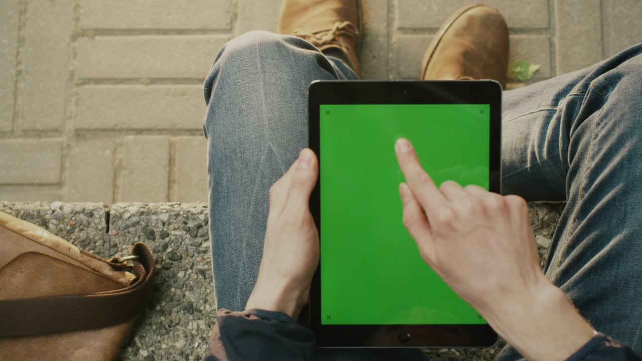 el hombre está usando la tableta en el regazo al aire libre en un día soleado.