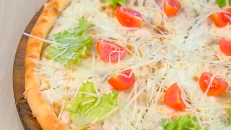 pizza with chicken and cheese, tomatoes and lettuce on top on wooden board.