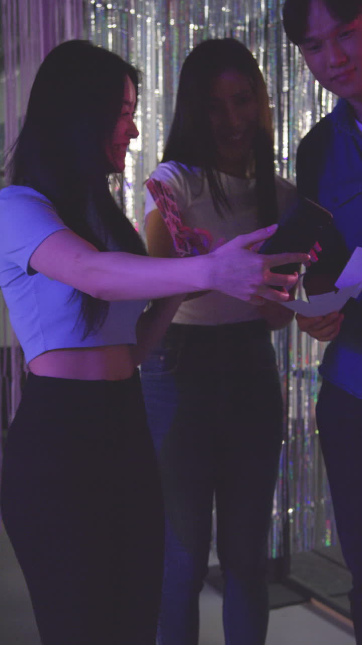 video vertical de un grupo de amigos tomando selfies divirtiéndose mirando las impresiones de la cabina de fotos en un club nocturno o feria