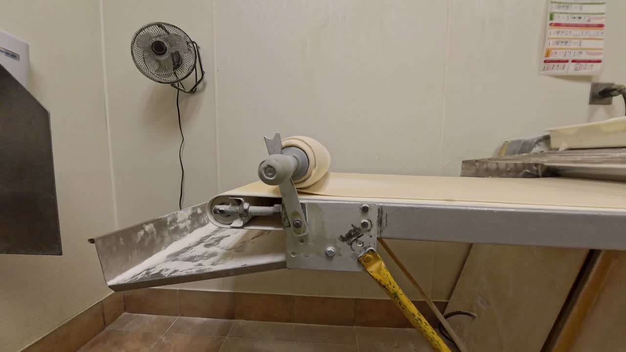 Raw dough rolling up onto a pin on a machine.