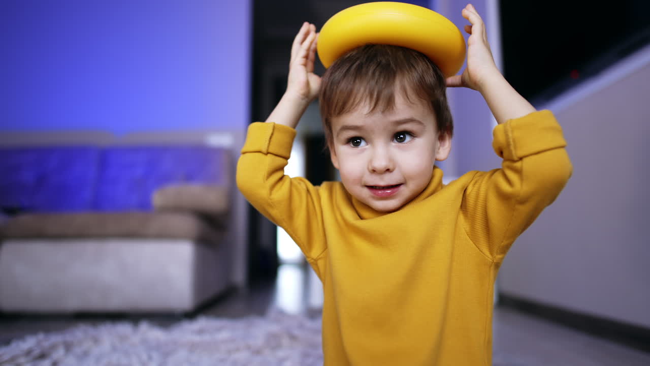 Lovely brown-haired baby in yellow sweater puts the toy ring on his head. Funny kid playing at home.