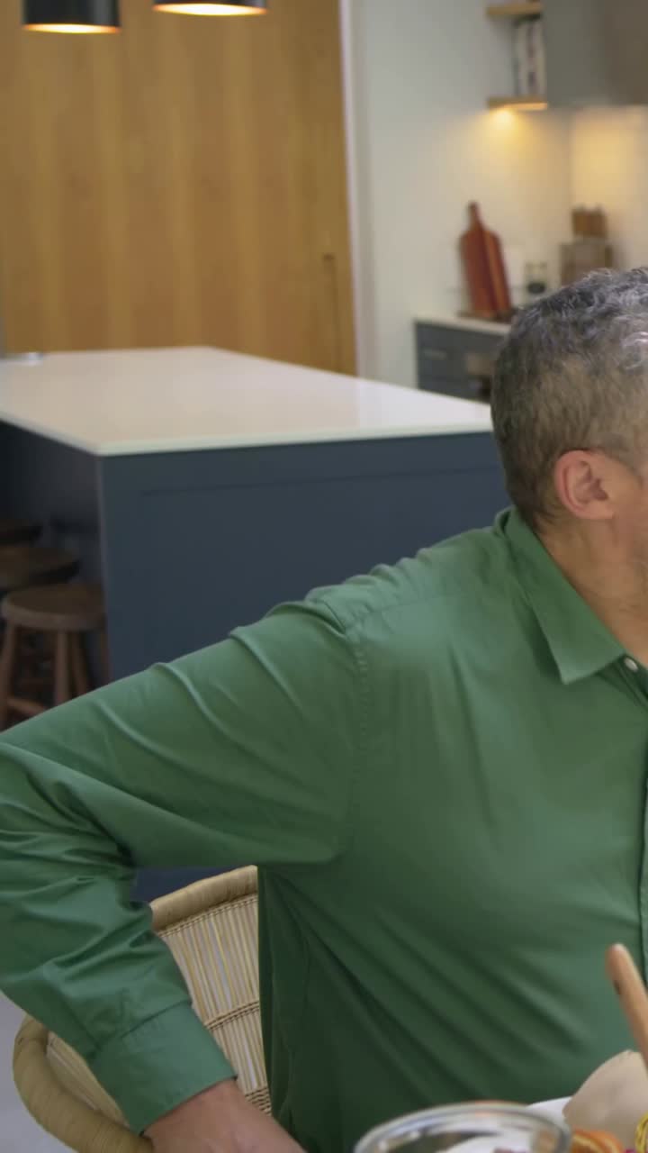 Vertical video: Pulling chair on arrival, man in green shirt sitting at kitchen table with salad