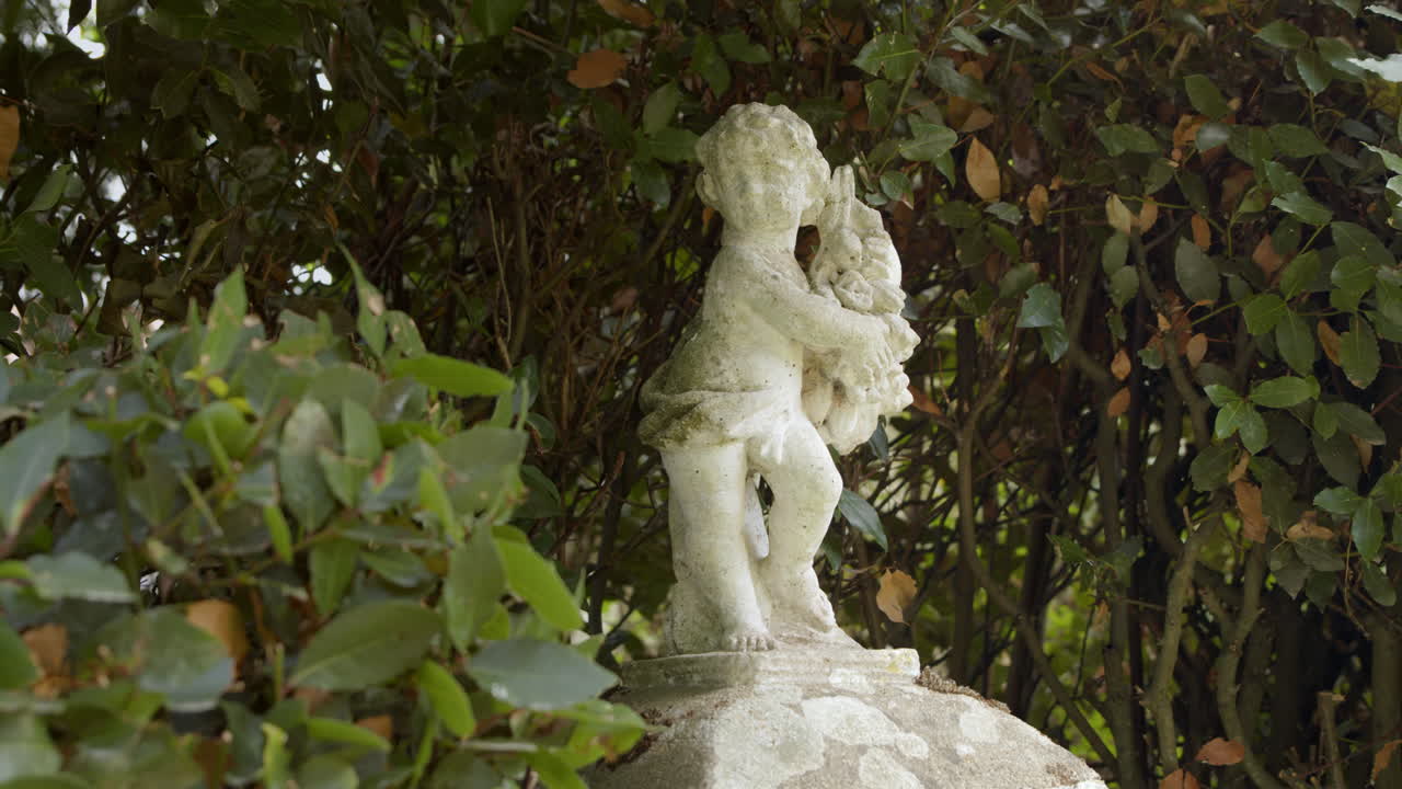 Primo piano con panoramica verso destra di una statua di angelo scolpita nel marmo in un parco in una giornata di sole.