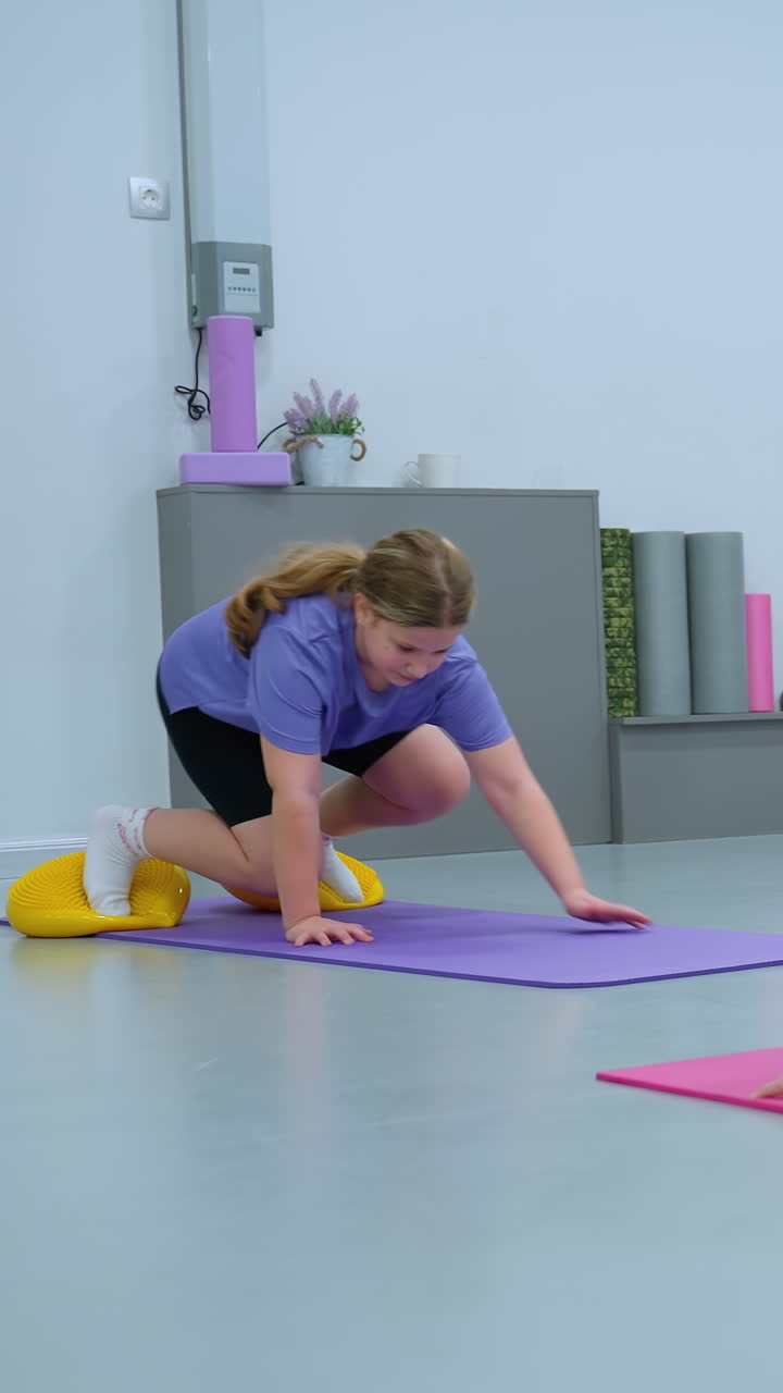 niños involucrados activamente en una sesión de entrenamiento vista a través de un espejo, un niño se equilibra en una pelota de ejercicio verde, otro se arrastra en una alfombra púrpura usando cápsulas de equilibrio amarillas