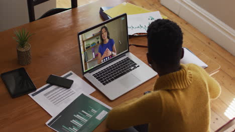 mujer afroamericana hablando y tomando notas mientras tiene una videollamada en una computadora portátil en casa