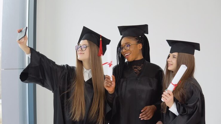 Three young happy students women of different nationalities stand together side by side and take a selfie with diplomas in their hands. Close up view on white background
