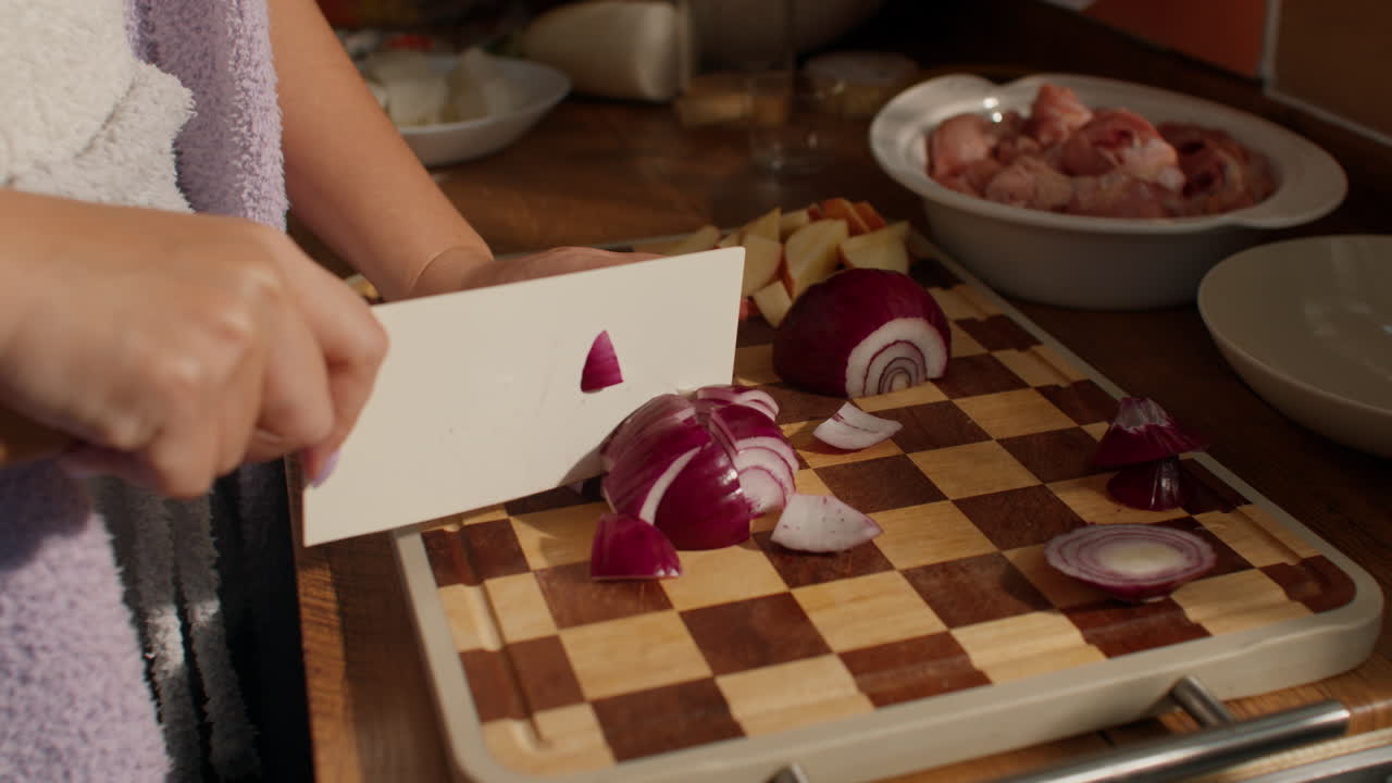 Person slicing red onion on a cutting board in a cozy kitchen setting