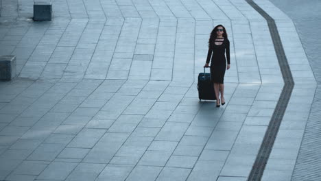 serious woman walking with suitcase on sidewalk