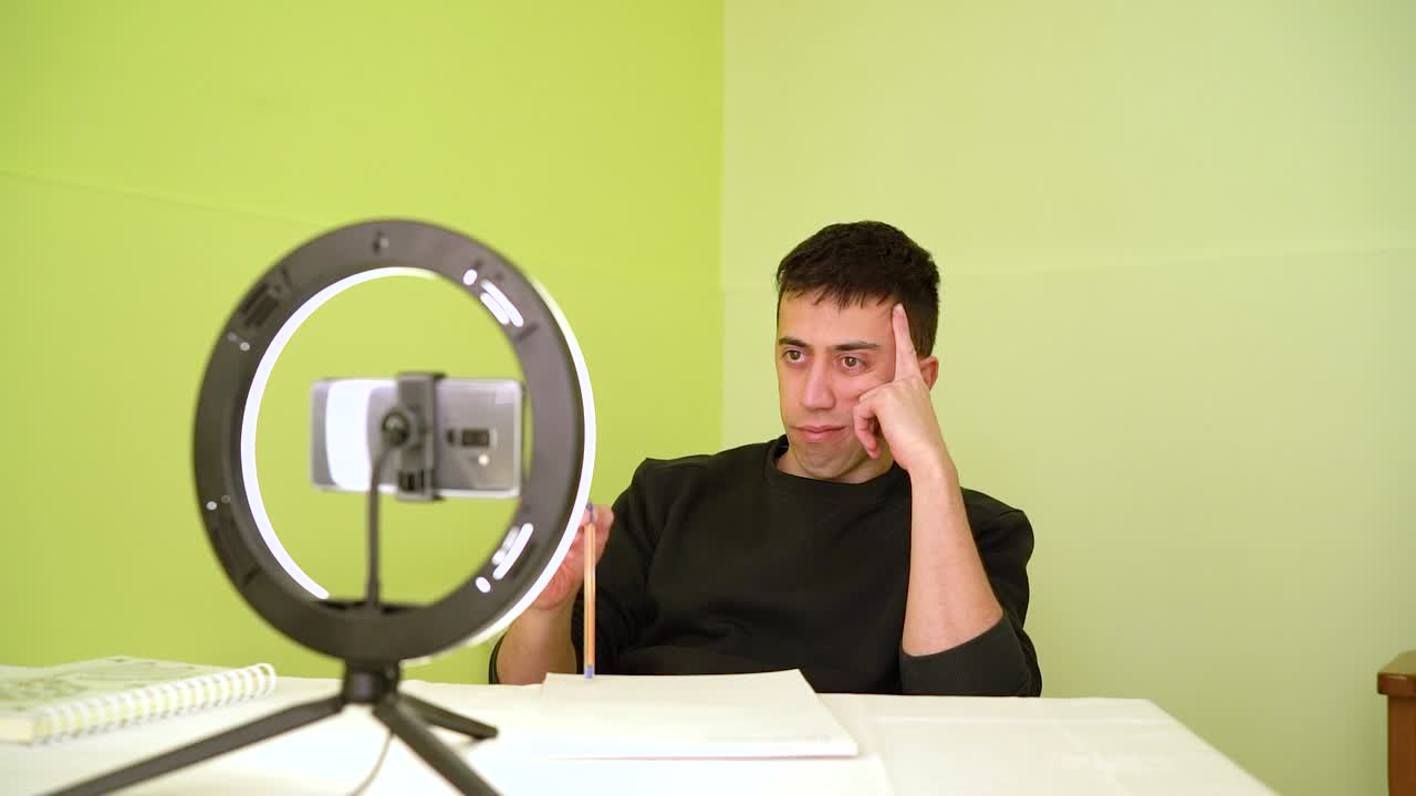 hombre milenario sintiéndose aburrido viendo video de clase en línea con cámara de teléfono celular en casa