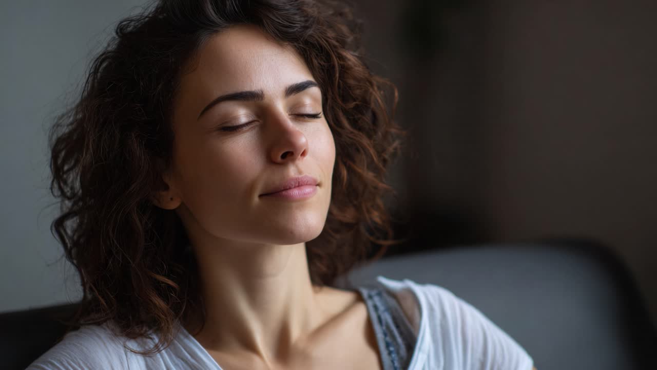 Un'espressione serena: una giovane donna con i capelli ricci che irradia calma e pace, immortalata in un momento di profondo relax e consapevolezza, in una stanza accogliente