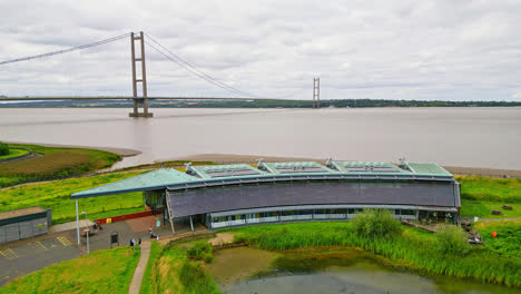 Witness-the-Waters'-Edge-Country-Park-and-Visitor-Centre,-set-against-the-iconic-Humber-Bridge,-from-a-breathtaking-aerial-perspective