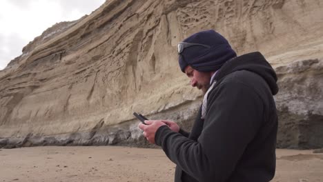 man looking at the remote control of a drone with a big rugged cliffs on the background