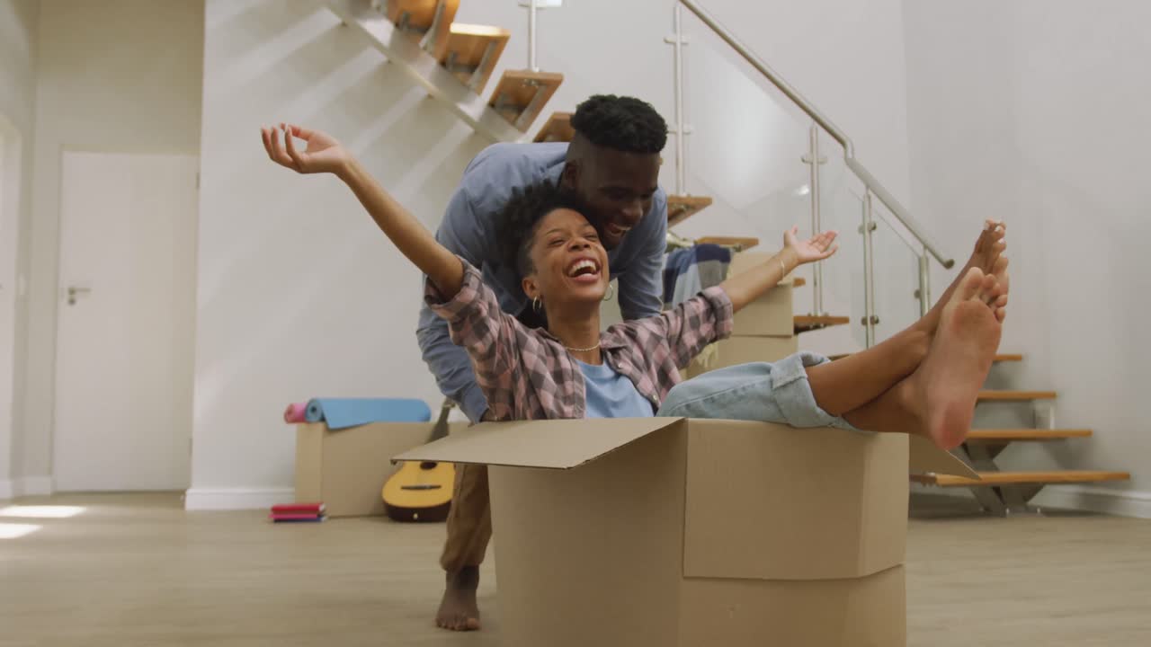 video de una feliz pareja afroamericana divirtiéndose con cajas después de mudarse a una casa nueva