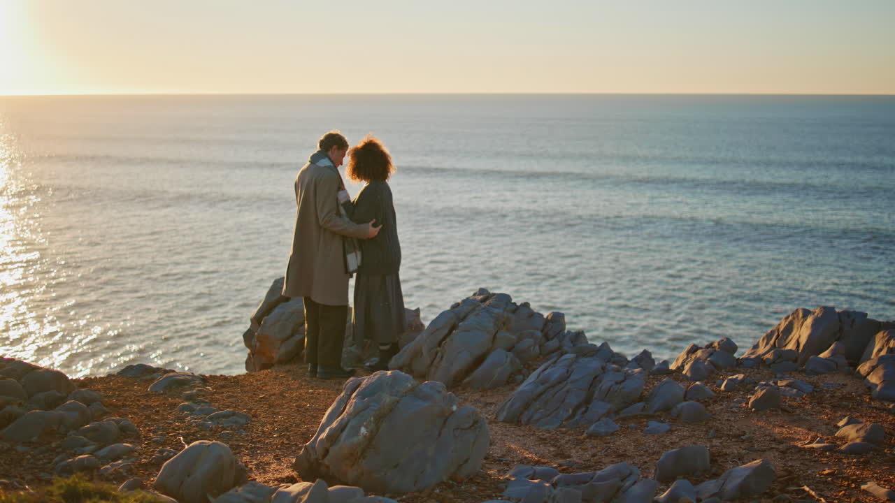 Serene pair watching sunset sky horizon hugging at sea shore. Spouses embracing