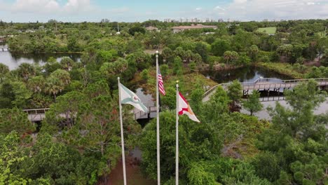 Toma-Aérea-De-Una-Bandera-Estadounidense,-De-Florida-Y-De-Nápoles-En-Ascenso-Frente-A-Un-Club-De-Campo-De-Lujo