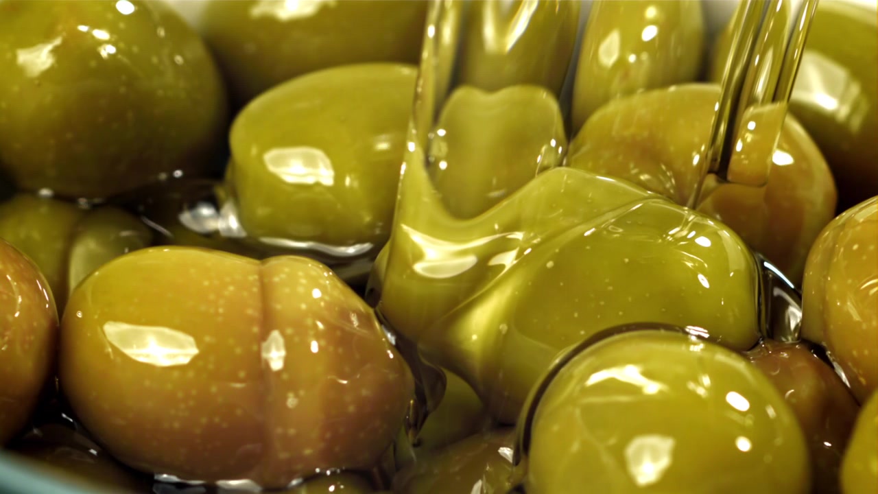 Primo piano di olio d'oliva versato su olive verdi fresche