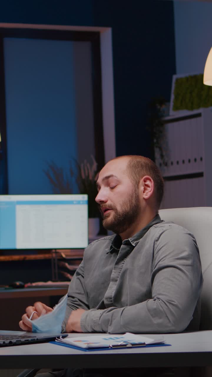 Vertical video Overworked businessman with face mask against covid19 working in startup office