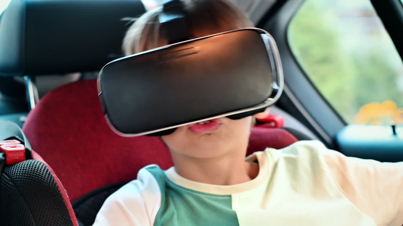 Boy sitting in the car and putting on VR glasses in child safety seat. Slow motion