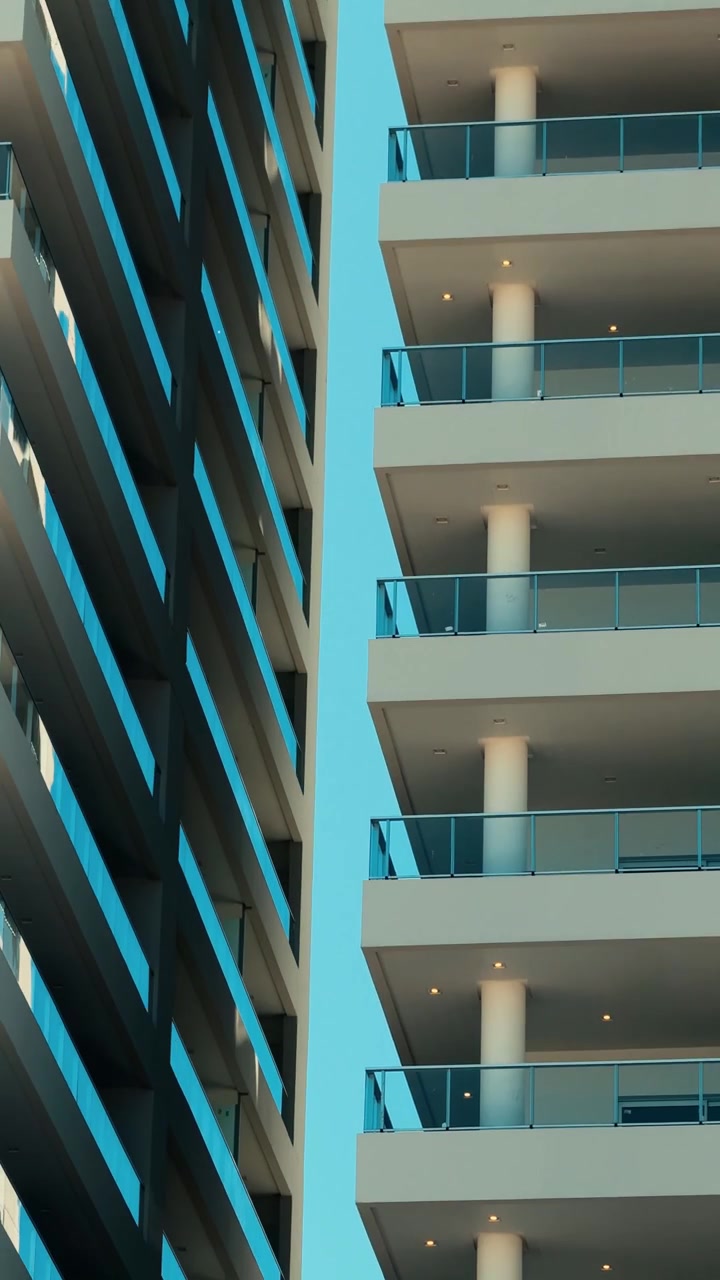 Panorámica vertical descendente de edificios modernos de gran altura con balcones y una palmera