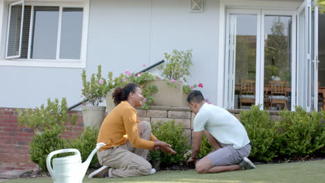 Feliz-Pareja-Gay-Diversa-Haciendo-Jardinería-Y-Hablando-Arrodillado-En-Un-Jardín-Soleado,-Cámara-Lenta