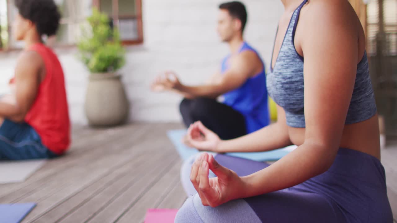 sección media de una mujer biracial practicando yoga con un grupo de amigos diversos en el patio trasero