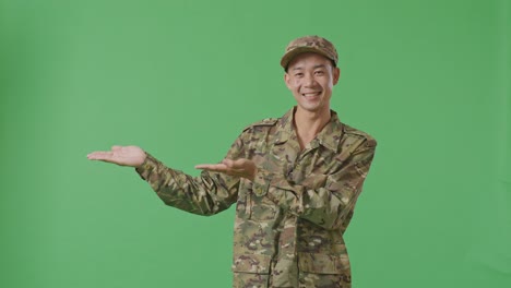 asian man soldier smiling and pointing to side while standing in the green screen background studio