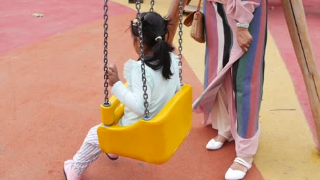 young girl playing on a swing at the playground with her mother