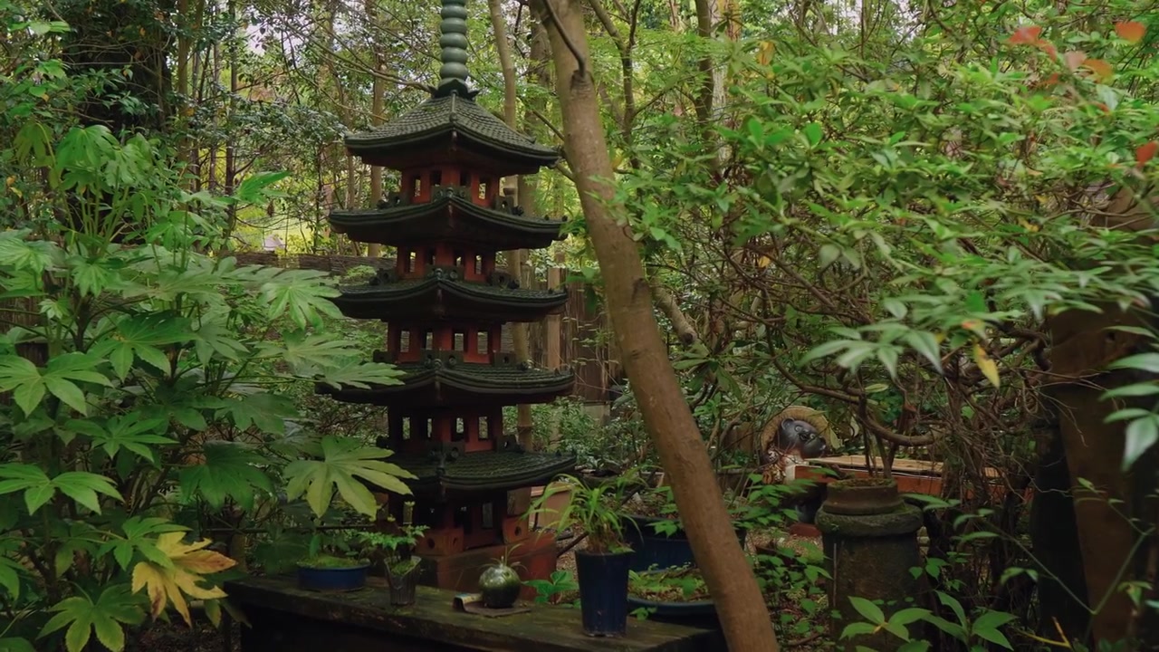 En høj træpagode står blandt tætte skovtræer i fredfyldte japanske omgivelser.