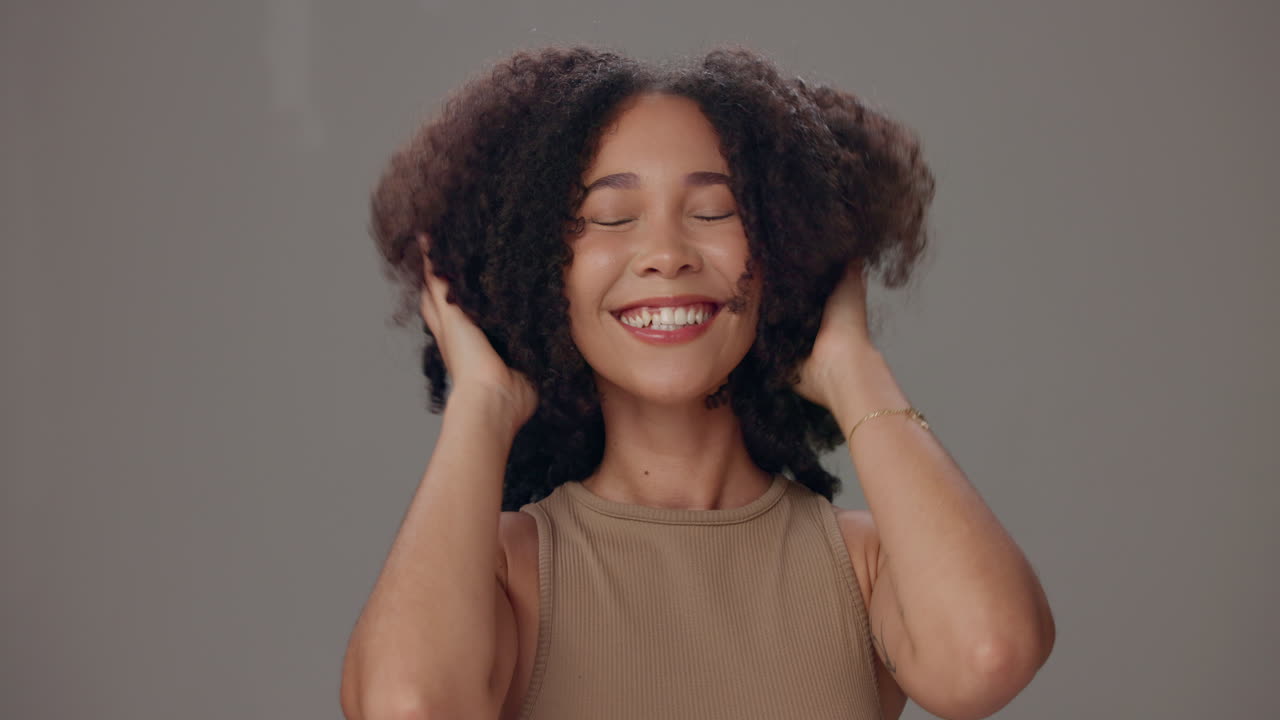 mujer feliz con el cabello rizado posando frente a un fondo gris