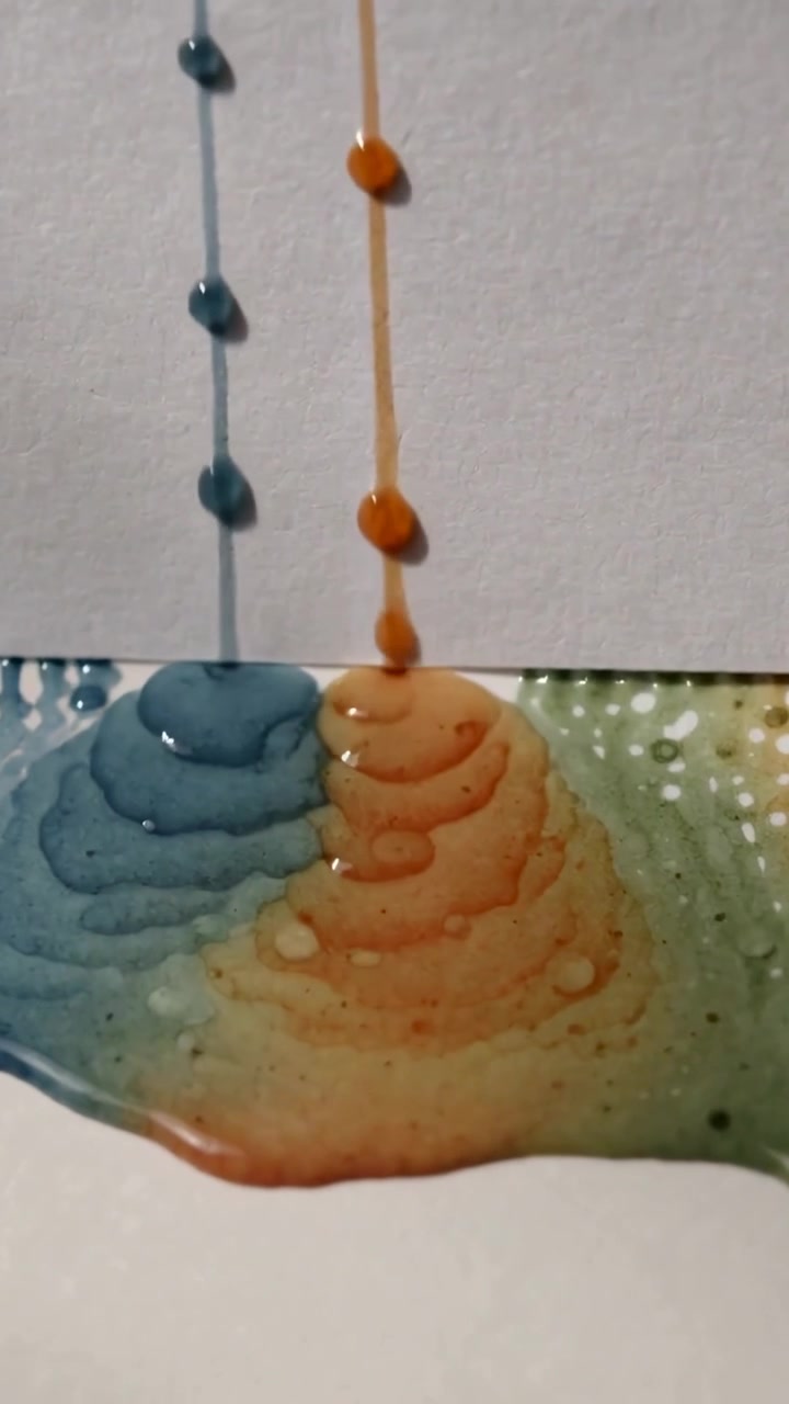 Video verticale: Gocciolamento da pipetta di flussi arancione-verde acqua che formano cumuli anulari su carta testurizzata