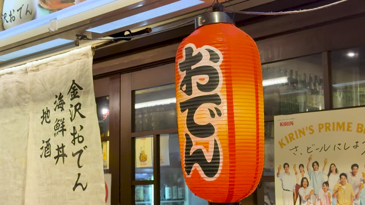 En lysende rød papirlanterne og et hvidt noren-gardin hænger udenfor en restaurant på Kanazawa-markedet