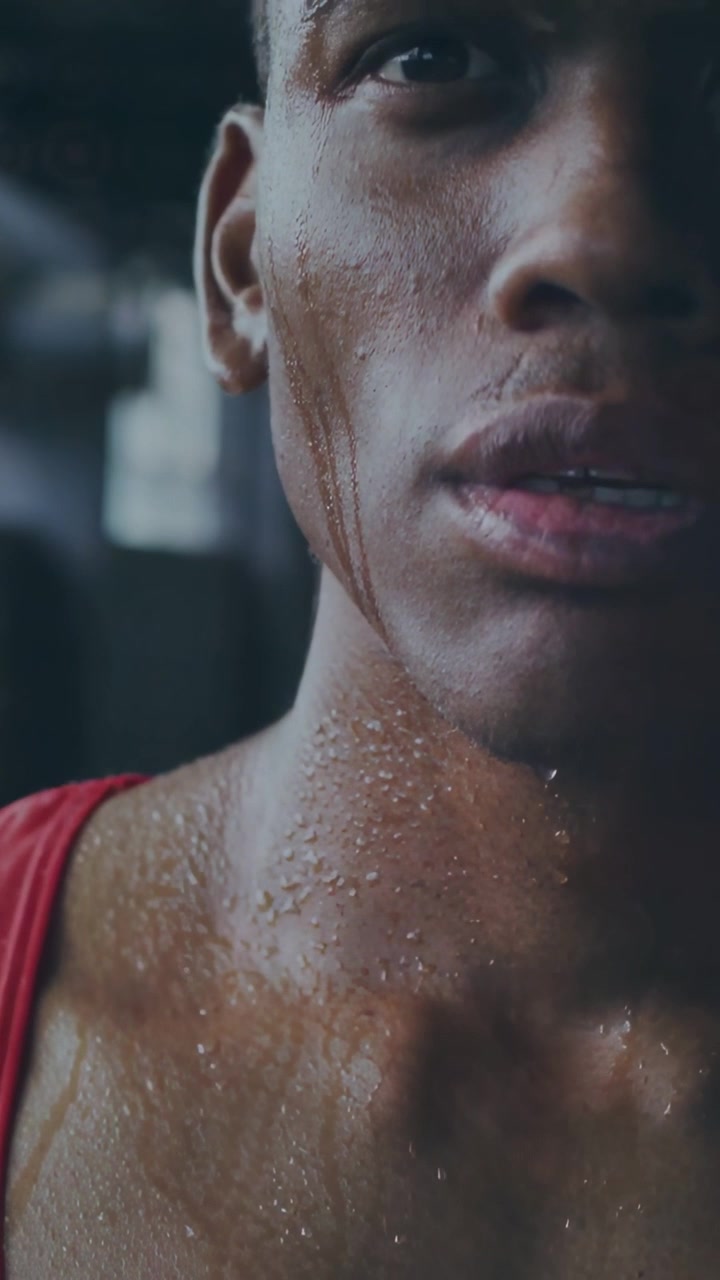 Video verticale: Telecamera che si muove verso l'alto mostrando un atleta maschio che respira, preparandosi in palestra, con il sudore che cola
