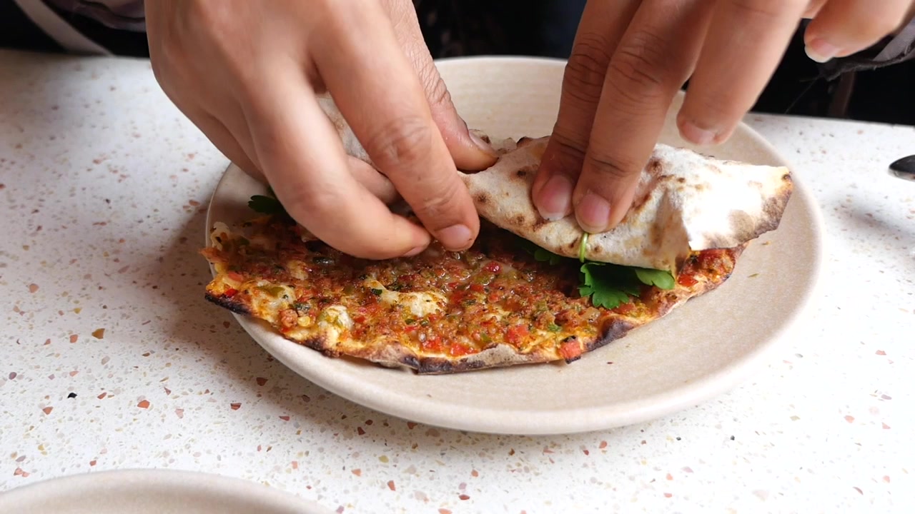 Person Rolling Lahmacun Flatbread with Fresh Herbs