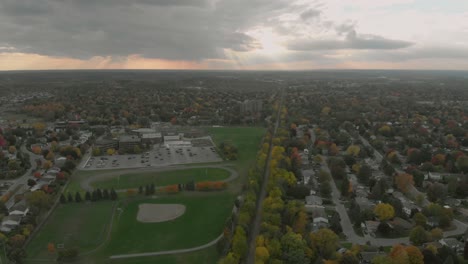 dynamic rising aerial footage following above a train track and facing a huge sunset with roads and vehicles in the distance and sun beams shimmering through the clouds